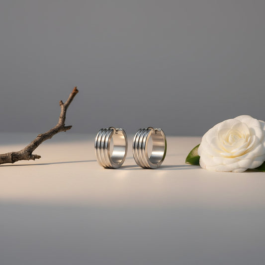 Aramat Jewels silver-tone stainless steel hoop earrings with three subtle vertical stripes, available in 13mm and 20mm diameters.