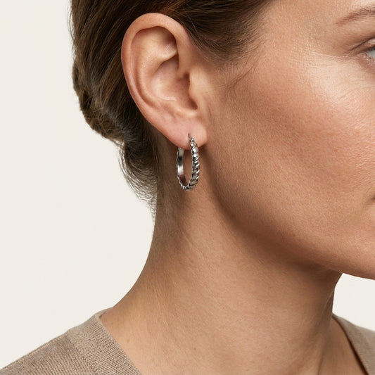 Aramat Jewels silver oval hoop earrings with diagonal stripe texture, 28mm diameter, worn by a model.