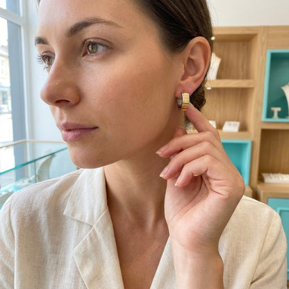 Aramat Jewels bicolor stainless steel hoop earrings with a gold stripe, 13x7mm, worn by a woman.