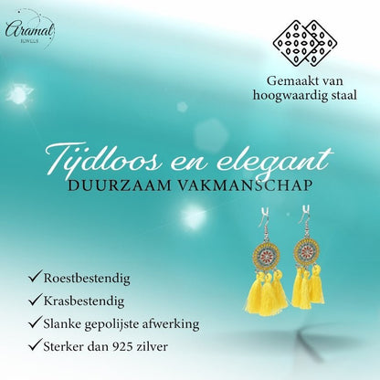 Aramat Jewels boho oorhangers met gele kwastjes en RVS details, gepresenteerd in een stijlvolle zomerse setting.