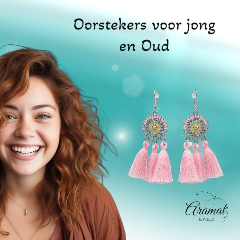 Lachende vrouw draagt Aramat Jewels boho oorhangers met licht roze kwastjes en emaille details in RVS.