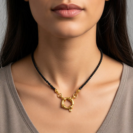 Aramat Jewels gold-tone stainless steel necklace with black seed beads and a circular clasp, worn by a model.