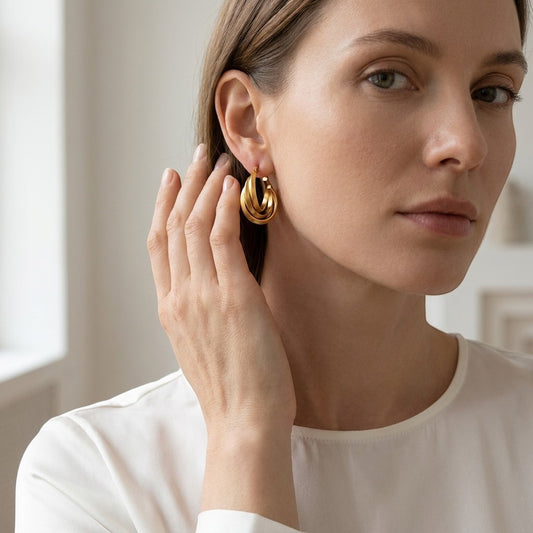Aramat Jewels triple gold-colored hoop earrings with a crossed design, 25x7mm, worn by a woman.