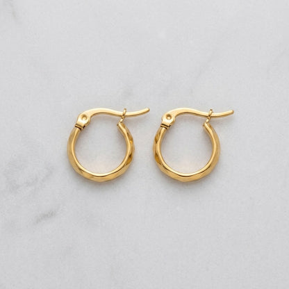 Aramat Jewels small gold-coloured stainless steel hoop earrings with faceted surfaces and a hinge closure.