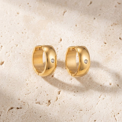 Aramat Jewels gold-tone stainless steel huggie hoop earrings with a central clear cubic zirconia stone.