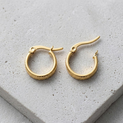 Aramat Jewels small gold stainless steel hoop earrings with a subtle striped pattern and hinge closure.
