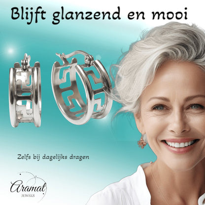 Aramat Jewels silver-tone stainless steel hoop earrings with Greek key design, 20mm diameter, worn by a smiling woman.
