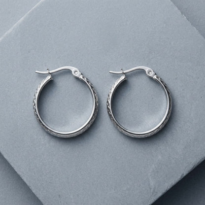 Aramat Jewels silver-tone stainless steel hoop earrings with a 30mm diameter and a subtle diamond pattern.