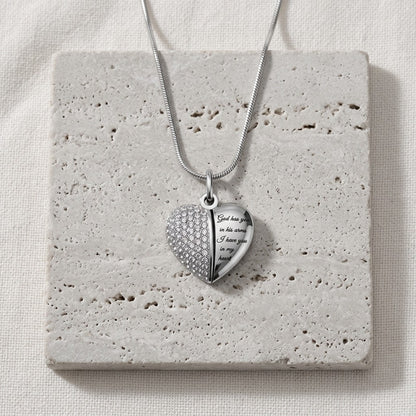 Aramat Jewels zilverkleurige stalen hartvormige ashanger met lila kristallen en gravure 'God has you in his arms, I have you in my heart'.