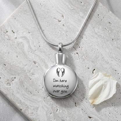 Aramat Jewels zilverkleurige stalen urnhanger met de tekst 'I'm here watching over you' en vleugels. Een troostend gedenksieraad.