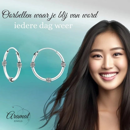 Aramat Jewels unisex silver Bali hoop earrings, 16mm diameter, with decorative bands. Model with dark hair smiles.
