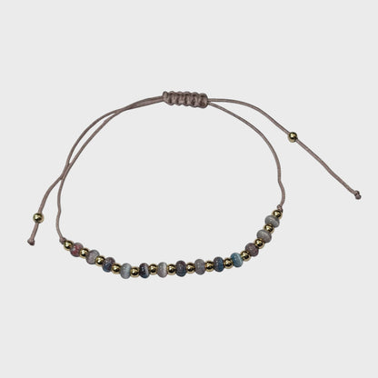 Aramat Jewels verstelbaar enkelbandje met grijze cats eye kralen en goudkleurige accenten op een taupe touwtje.