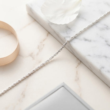 Aramat Jewels zilverkleurige slangenketting van roestvrij staal op een marmeren ondergrond met een bloemblad.