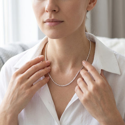 Aramat Jewels zilverkleurige slangenketting van roestvrij staal gedragen door een vrouw in een wit overhemd.