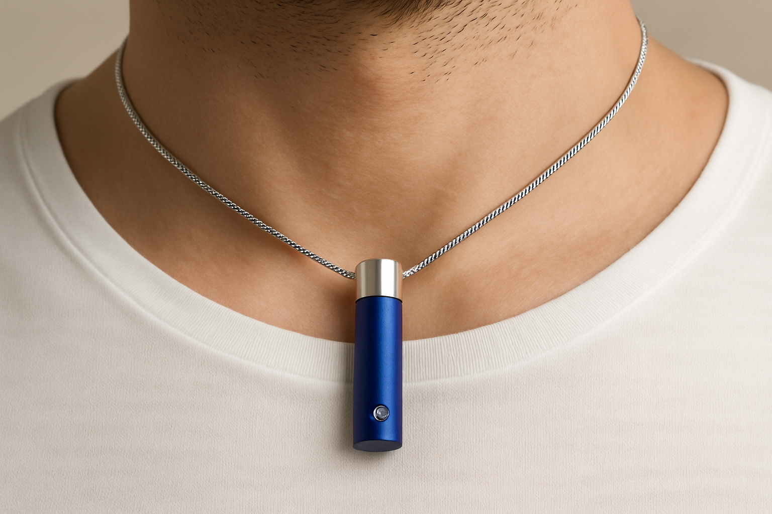 Blauw-zilveren cilindrische ashanger, 36x12mm, met geborsteld blauw metalen lichaam, zilveren dop bovenaan, en kleine diamant accent. De zilveren slangenketting loopt door het midden van de cilinder, gedragen op mannenhals.