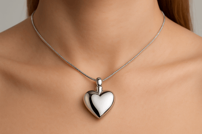 Zilveren massieve hartvormige ashanger, 28x20mm, hoogglans afwerking, gedragen op vrouwenhals met zilveren slangenketting. Elegante gedenksieraad voor asresten, tijdloos rouwsieraad in hartvorm.