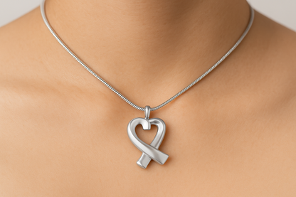 Zilveren hartvormige ashanger met lint-ontwerp, 30x17mm, gedragen op vrouwenhals met zilveren slangenketting. Hoogwaardige gedenksieraad voor asresten, rouwsieraad in hartvorm, elegante ashanger zilver.