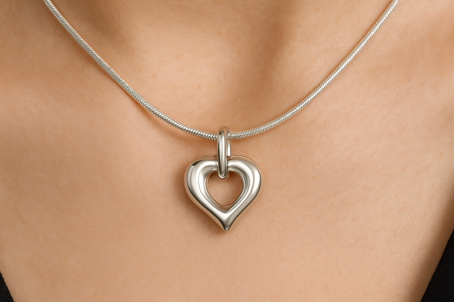 Zilveren open hartvormige ashanger, 25x20mm, met gladde afgeronde randen, puntige onderkant en ovale ring bovenaan, precies zoals het origineel, gedragen op vrouwenhals met zilveren slangenketting.